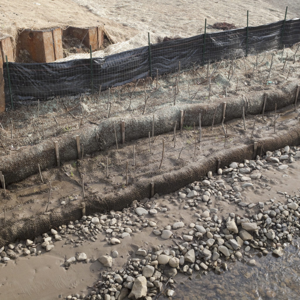 Erosion control measures using burlap, plastic fencing, steel beams, wood stakes and new plantings.